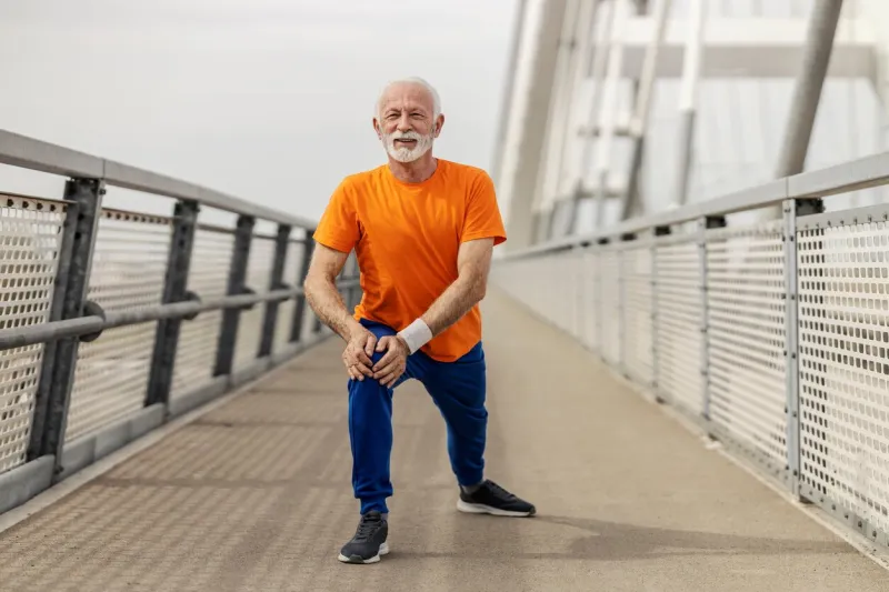 smiling fit senior sportsman stretching his leg on a bridge and doing warmup exercises