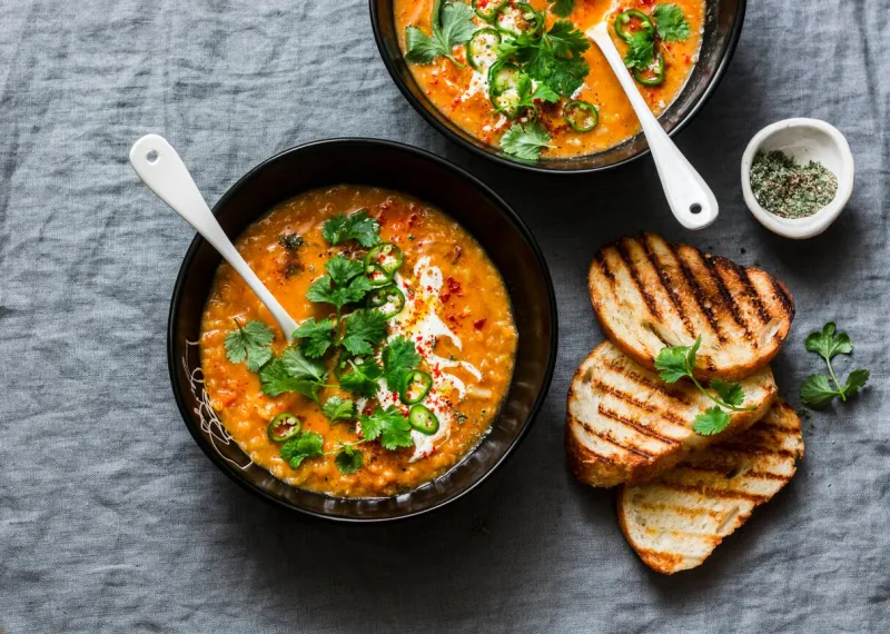 curried red lentil tomato and coconut soup - delicious vegetarian food on grey background, top view flat lay served healthy lunch