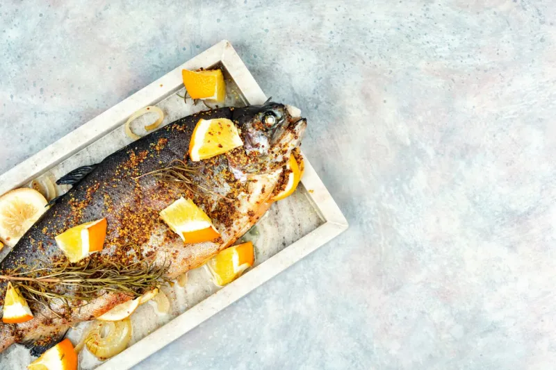 delicious roasted trout seasoned with spices and orange on a stone serving board copy space