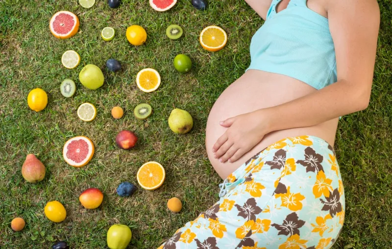 pregnant woman is laying on grass with fruit
