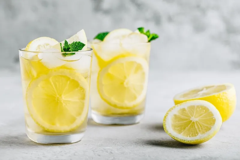 lemonade with lemon, mint and ice cubes in glass on gray stone background cold summer refreshing drink or beverage