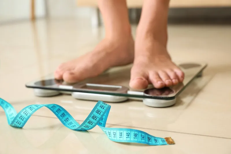 tape in front of woman standing on floor scales indoors overweight problem