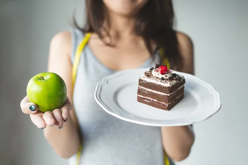 choose right food for you health person eat dessert holding green apple and cake to compare calories as sweet menu to eat during diet