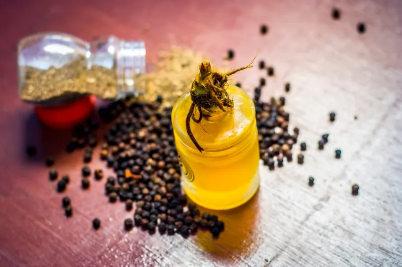 close up of oil of black pepper,piper nigrum with raw black pepper and powder on a wooden surface