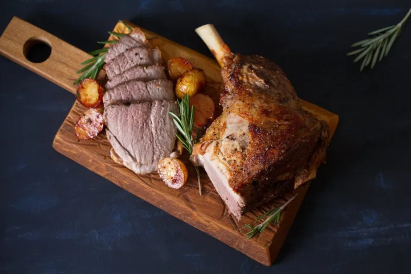 roast leg of lamb with potatoes and rosemary on dark background overhead, flat lay, horizontal image