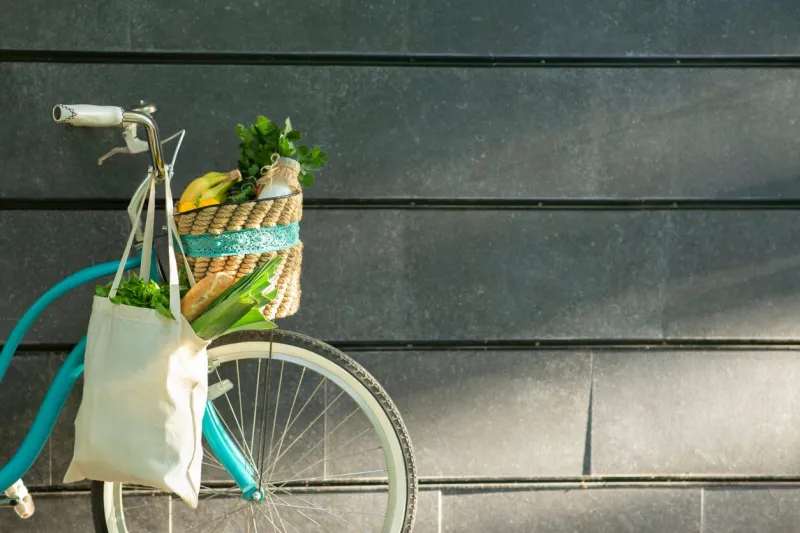 eco friendly bicycle with organic vegetables in cotton reusable bag over concrete wall, copy space