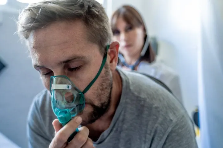young sick man patient with oxygen mask while female doctor listens his chest with stethoscope in hospital emergency room in smoking, respiratory diseases and health care anti tobacco advertising campaign