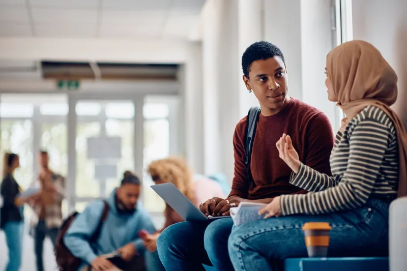 multiracial student couple communicating in hallway at the university focus is on african american student using laptop