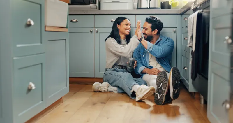 couple, coffee and sitting on floor in kitchen for quality time or fun to celebrate or discussion love, smile and woman with high five are bonding together with caffeine and conversation or care