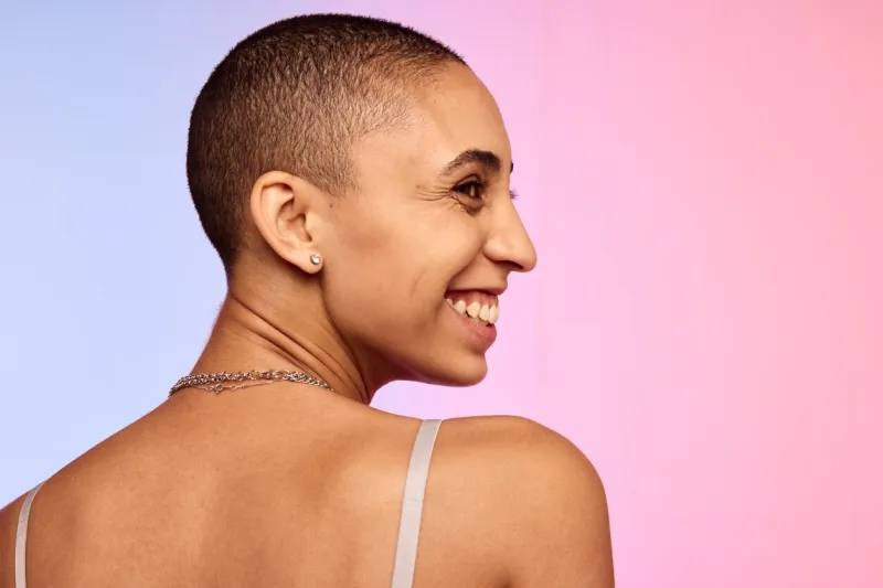smiling woman with shaved head rear view of androgynous female looking away and smiling on colorful background
