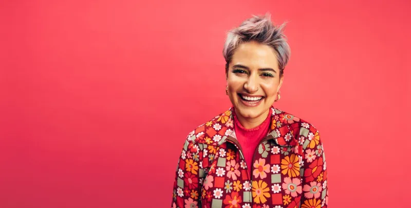 hipster woman looking at the camera with a happy smile on her face cheerful young woman standing alone against a red background fashionable young woman with dyed hair feeling vibrant