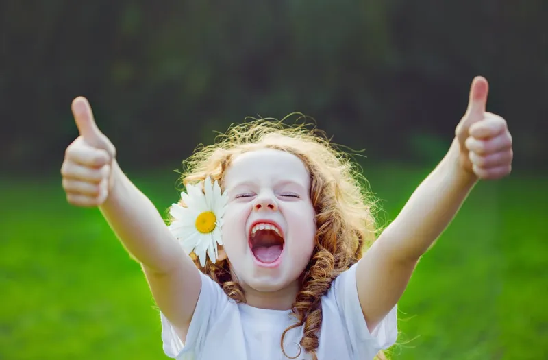 laughing girl with daisy in her hairs, showing thumbs up