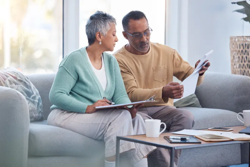 finance, documents and senior couple on sofa with bills, paperwork and insurance checklist in home, life or asset management, elderly black people on couch with financial, retirement or mortgage debt