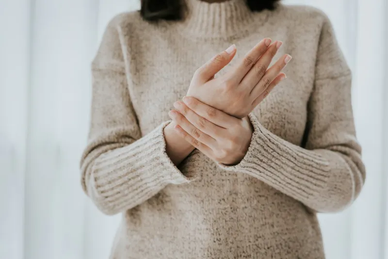 cropped shot of woman in sweater holding her wrist pain