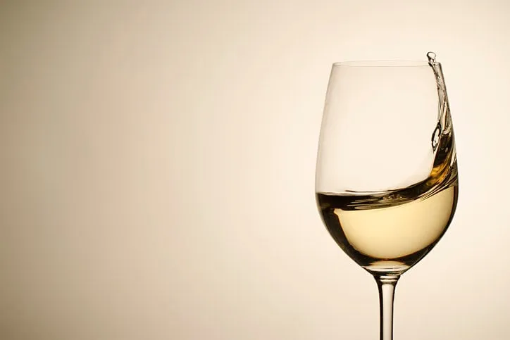 suspended droplets and splash of white wine in a stylish wineglass in a close up side view on a neutral background with copy space