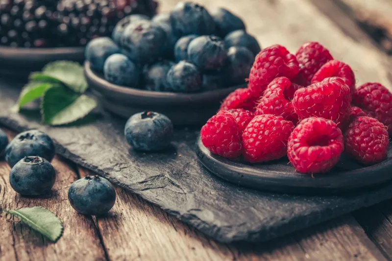fresh berries with raspberries, blueberries, blackberries in bowl on a stone stand on wood background