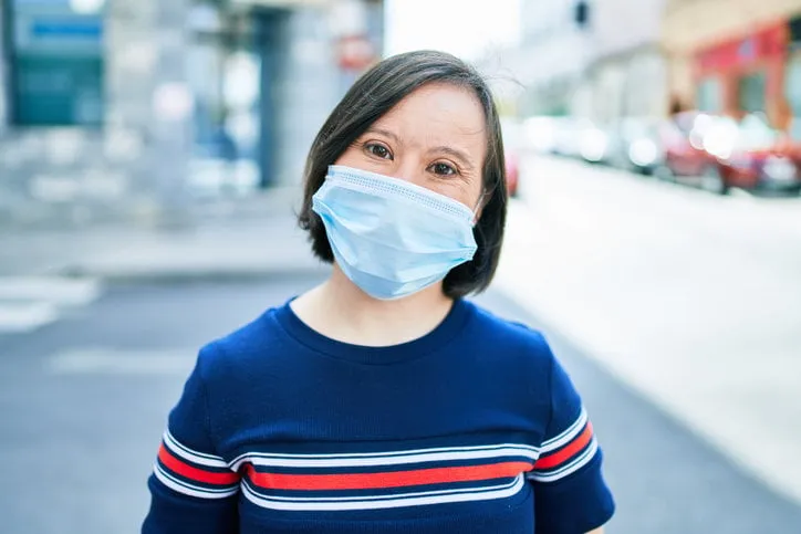 beautiful brunette woman with down syndrome at the town on a sunny day wearing safety medical mask for coronavirus