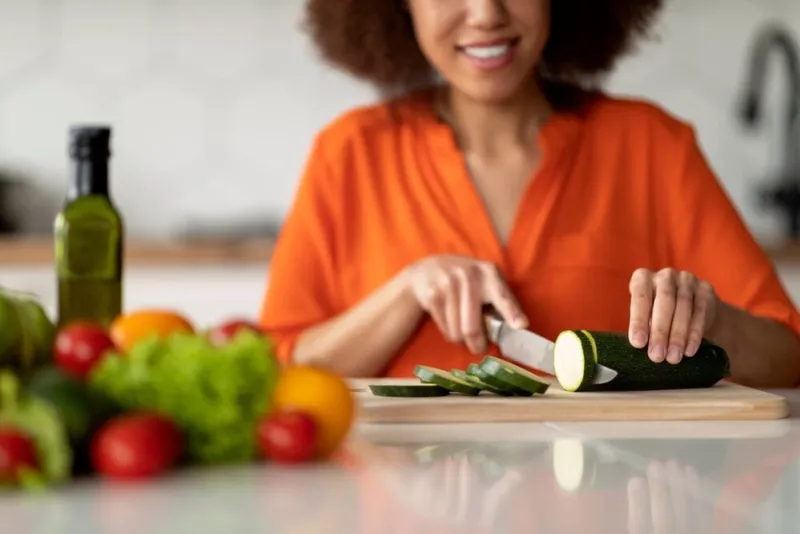 smiling,black,woman,chopping,zucchini,courgette,while,cooking,meal,in