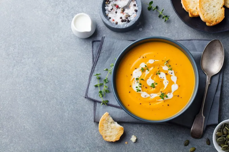 pumpkin, carrot cream soup in a bowl grey background top view copy space