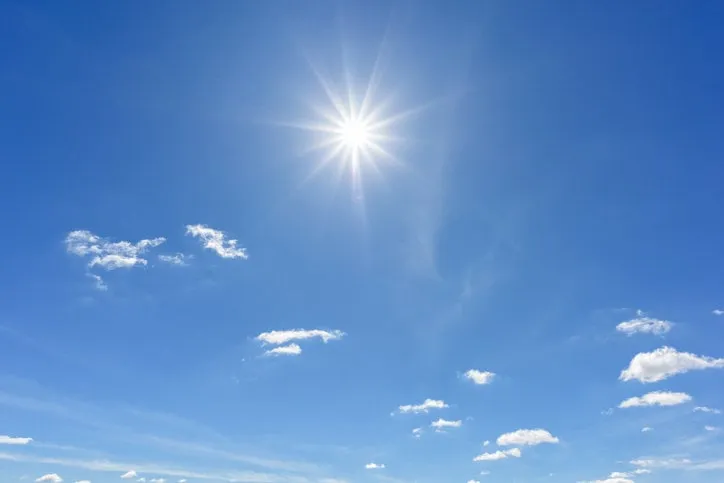 blue sky with clouds and sun reflection looking up view