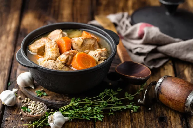 meat stewed with carrots in sauce and spices in cast iron pot on dark wooden rustic background