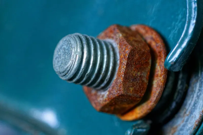 gray bolt and rusty brown nut on a green metal wall