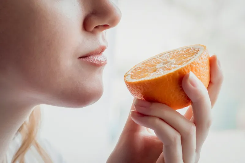 loss of smell concept close up portrait of caucasian young woman stands near the window and sniffs an orange