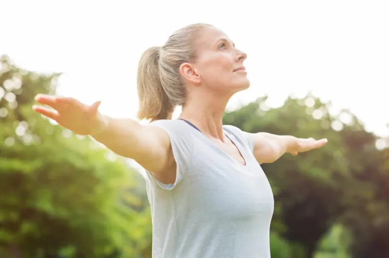 mature woman doing yoga at park and looking away senior blonde woman enjoying nature during a breathing exercise portrait of a fitness woman stretching arms and looking away outdoor r