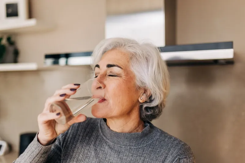 elderly woman drinking fresh tap water from a glass grey-haired mature woman staying healthy and hydrated at home