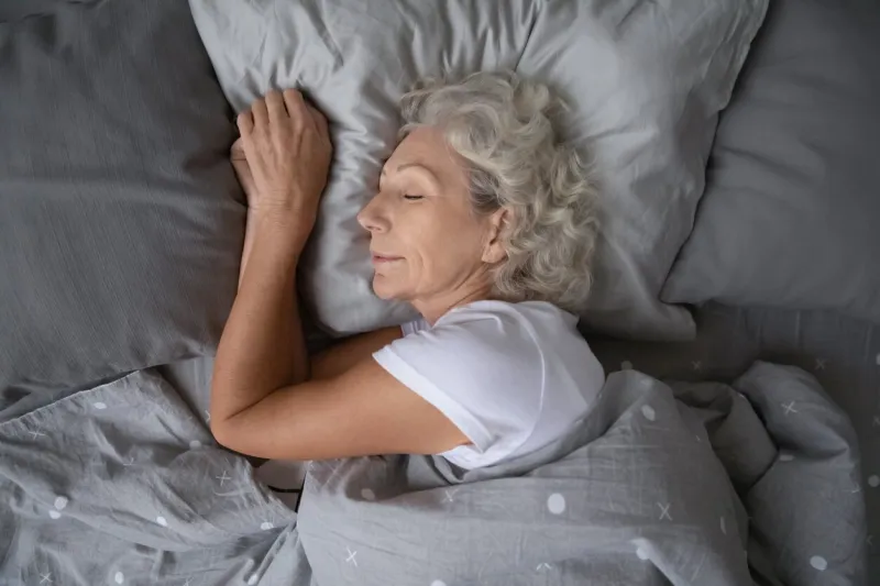 above top view calm peaceful elderly mature hoary woman sleeping on soft pillow under blanket, enjoying sweet dreams at night happy middle aged granny lying on side, resting in comfortable bed alone