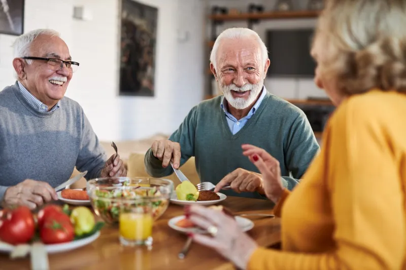 group of happy senior friends talking while having a meal at dining table