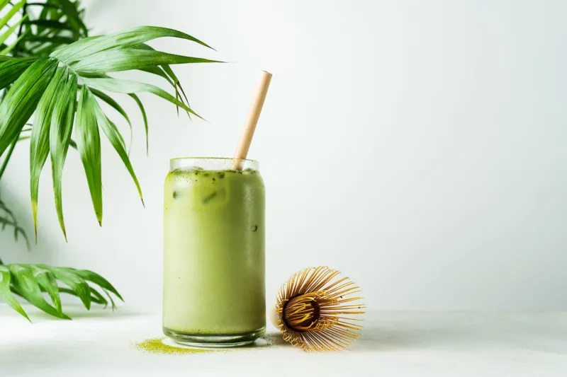 making japanese iced matcha latte, green tea with milk, soy milk, traditional matcha tools, with bamboo straw in glass on white background