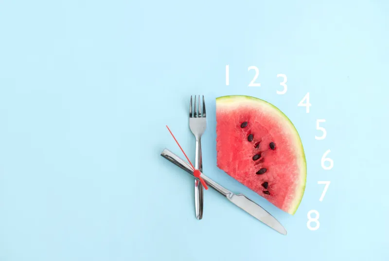 watermelon with cutlery as clock hands, eight hour intermittent fasting diet concept