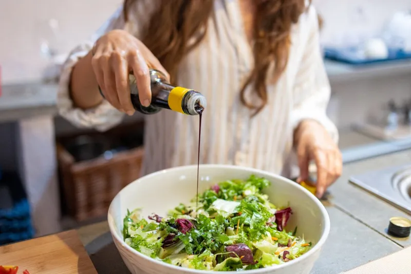 female hand pouring balsamic vinegar on the fresh vegetables salad