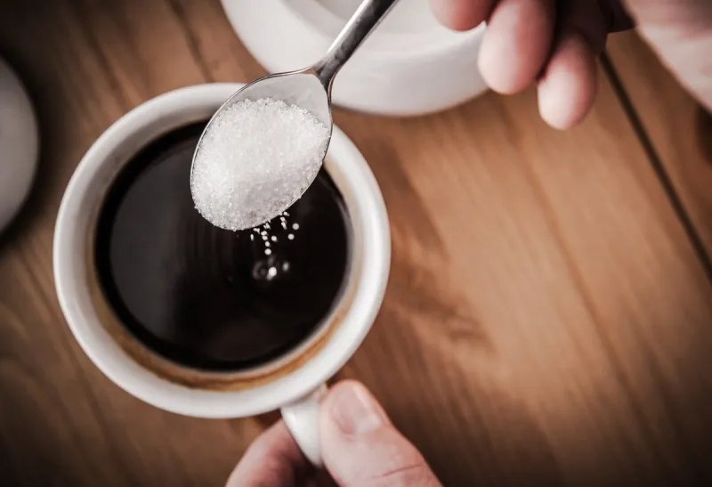 adding sugar to cup of black coffee sweetening using cane sugar