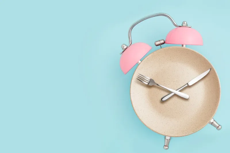 alarm clock and plate with cutlery concept of intermittent fasting, lunchtime, diet and weight loss