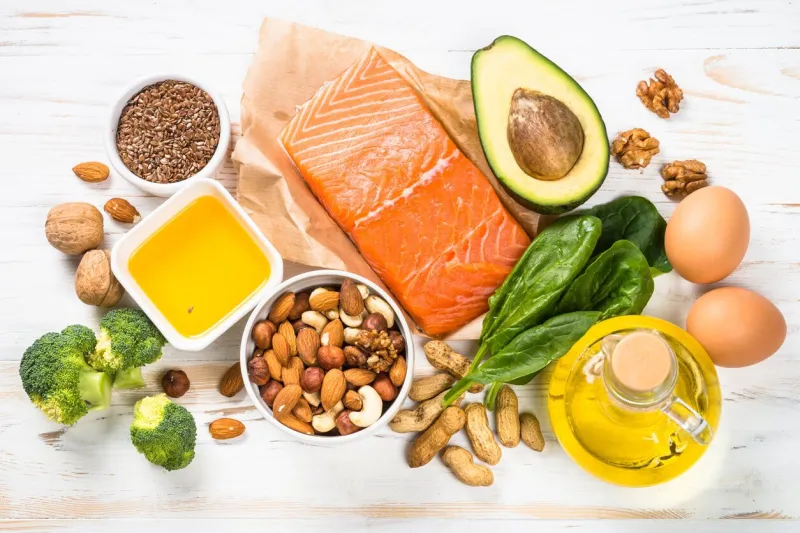 keto diet product at white wooden table salmon, olive oil, avocado, eggs, nuts and vegetables healthy food