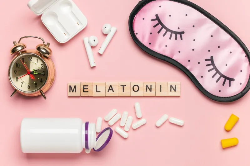 white bottle and pills, letters melatonin, alarm clock and sleep mask on light grey background sleeping backdrop concept melatonin, insomnia and good night top view