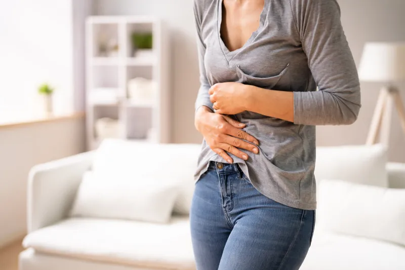 woman sitting on sofa suffering from stomach pain