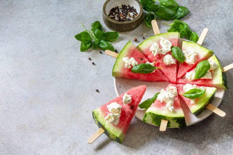 healthy seasonal dieting and nutrition, summer snack watermelon pizza with feta cheese and basil on a gray stone tabletop copy space