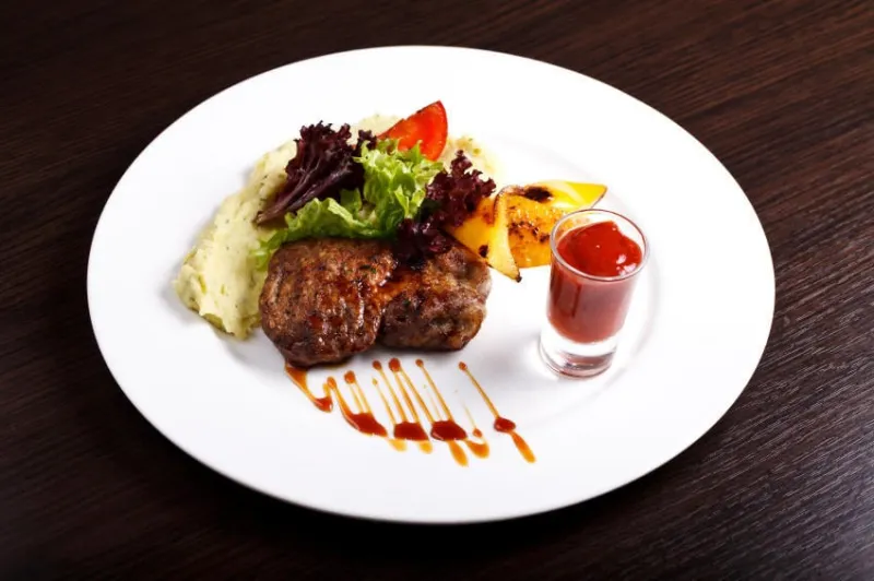 un plat avec de la viande, des pommes de terre et des herbes sur une plaque blanche