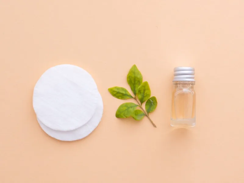 natural cosmetics fresh green leaves, cotton pads, body shower gel or liquid handmade soap or face cleanser isolated on a nude color skin background minimalistic design flat lay top view copy space