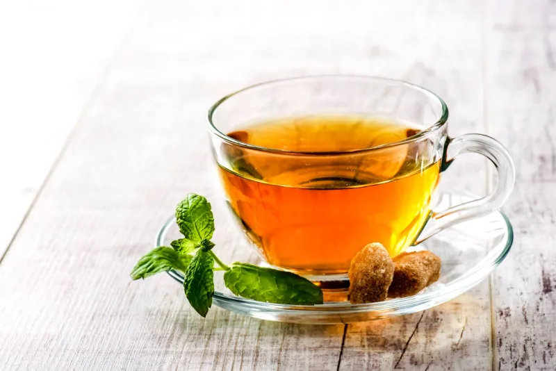 hot cup of tea on white rustic table tea in clear glass on white with sugar and mint leaf