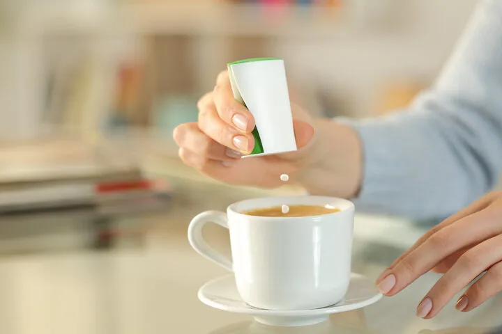 close up of woman hand throwing saccharin pills on coffee cup on a desk at home