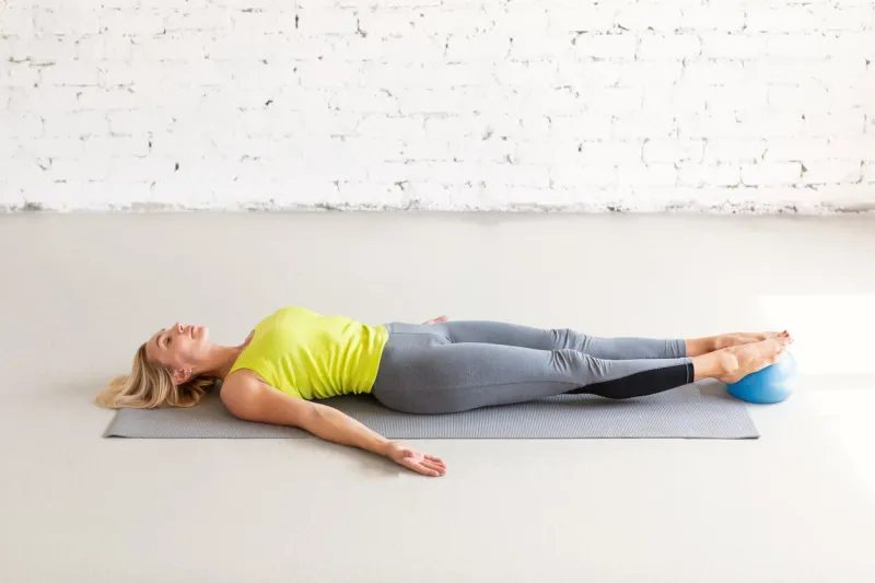 relaxation pose in pilates class caucasian woman lying on the mat in shavasana with a small fit ball under her feet in the loft studio indoor, selective focus workout, recovery, pelvic floor and leg relax, recreation and health concept