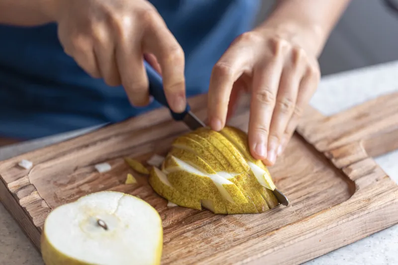 a woman cuts a pear into small pieces on a wooden cutting board, close-up