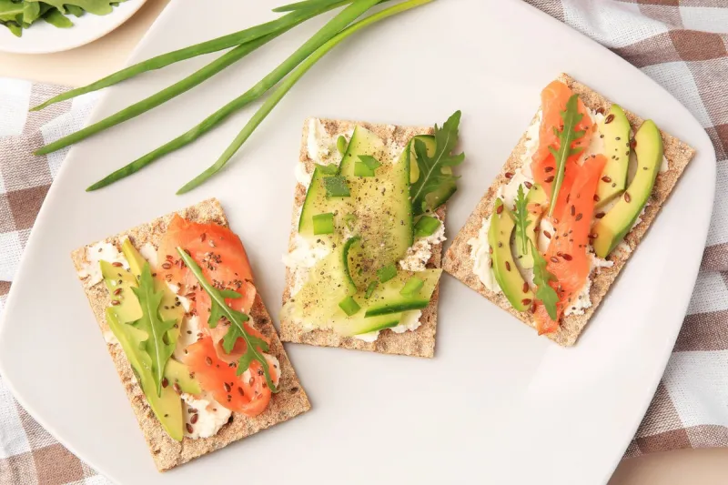 fresh crunchy crispbreads with cream cheese, cucumber, green onion, salmon and arugula on plate, flat lay