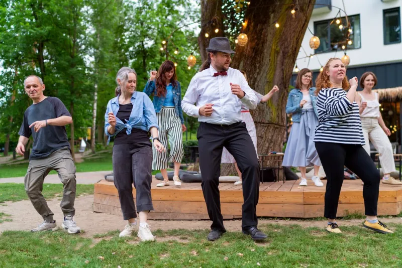 cheerful dance party outdoors, featuring individuals of different ages enjoying the festive ambiance under illuminated string lights they are dancing swing dance in summer city park