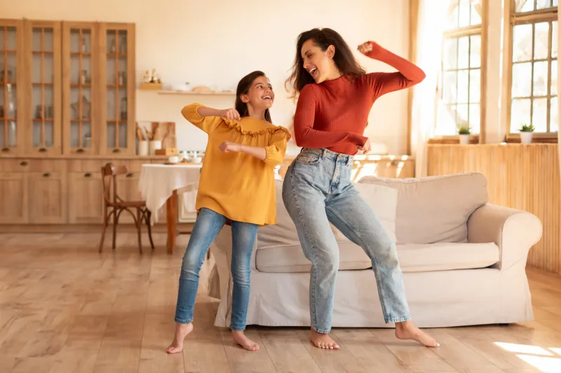 positive arab young mom and preadolescent daughter dancing together standing in modern home interior, haivng fun on weekend kid and mom fooling during domestic party for two, full length