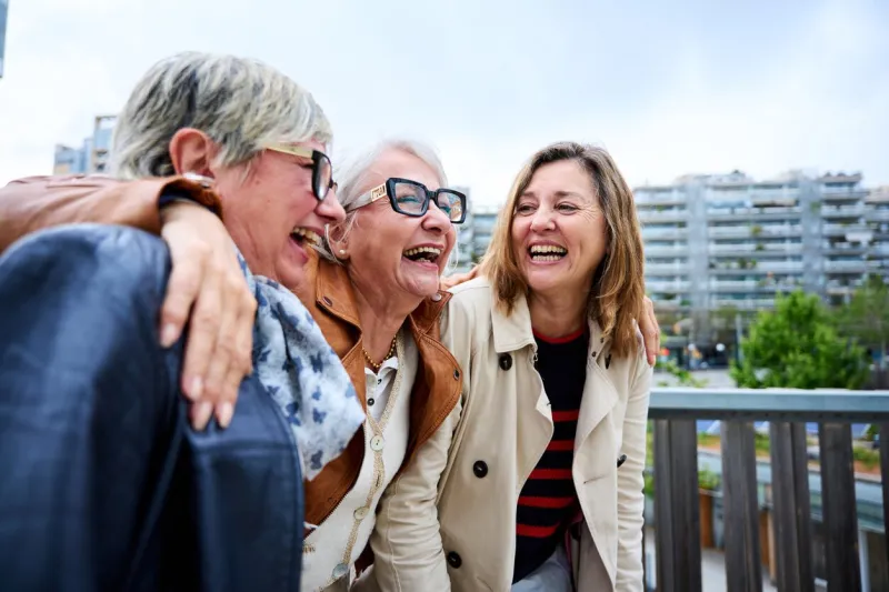 group of three mature caucasian women enjoying embracing walk together laughing outdoor senior female friends having fun hugging strolling happy in the urban city street elderly people enjoying